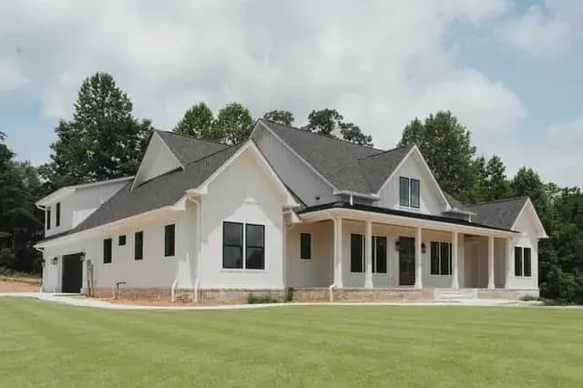 Three-quarter view showing the symmetric gable rooflines, black-framed windows, and full-width covered front porch with cedar beam detailing