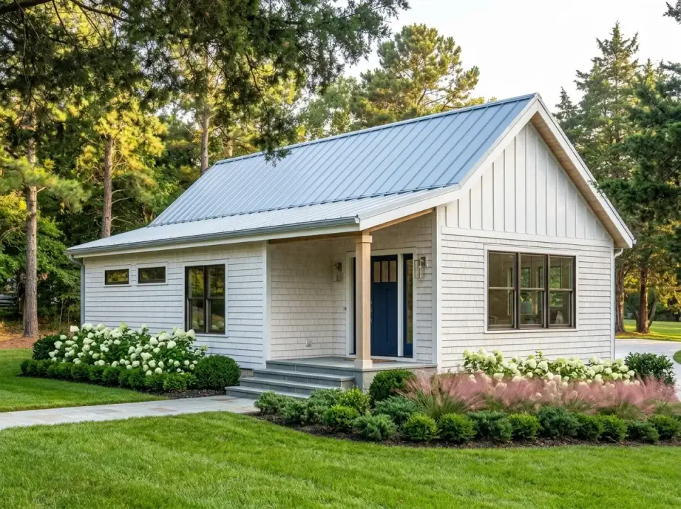 Coastal shingle cottage facade with light shingle siding, pale blue front door, silver metal roof and hydrangea masses around foundation