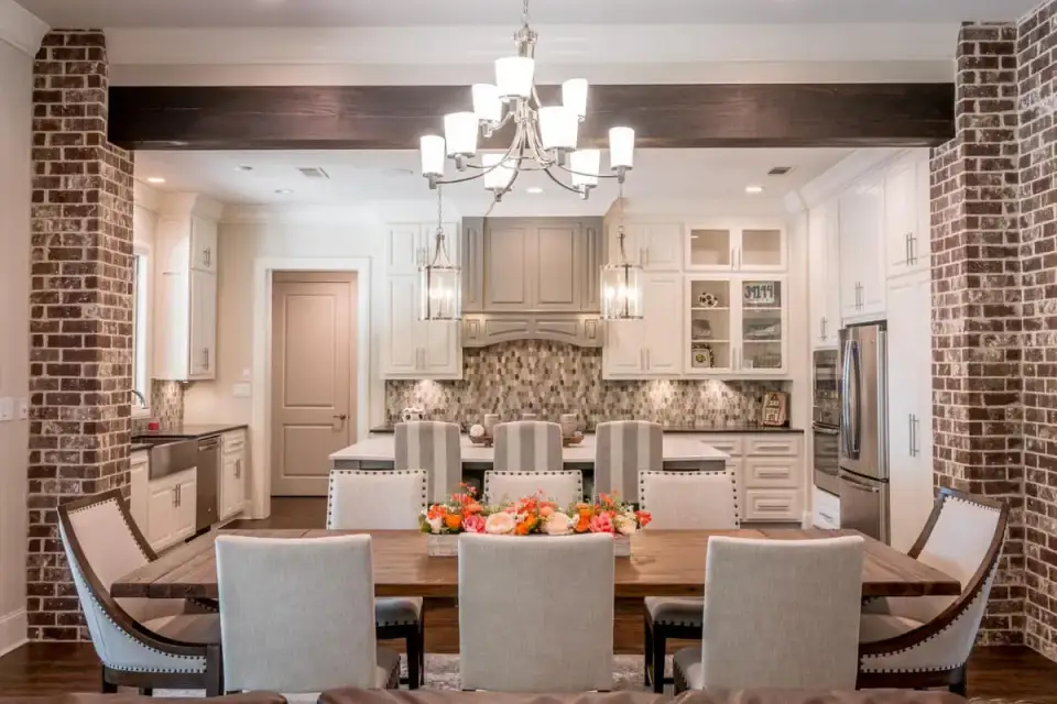 Kitchen interior showing a large quartz island, distinctive whitewashed brick arch framing the Wolf 48-inch dual-fuel range and hood, custom painted cabinetry, and pendant lighting from Visual Comfort over the island