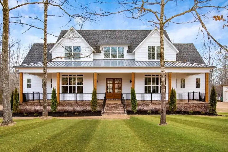 Three-quarter exterior view showing board-and-batten siding, metal porch roof, and stone veneer foundation