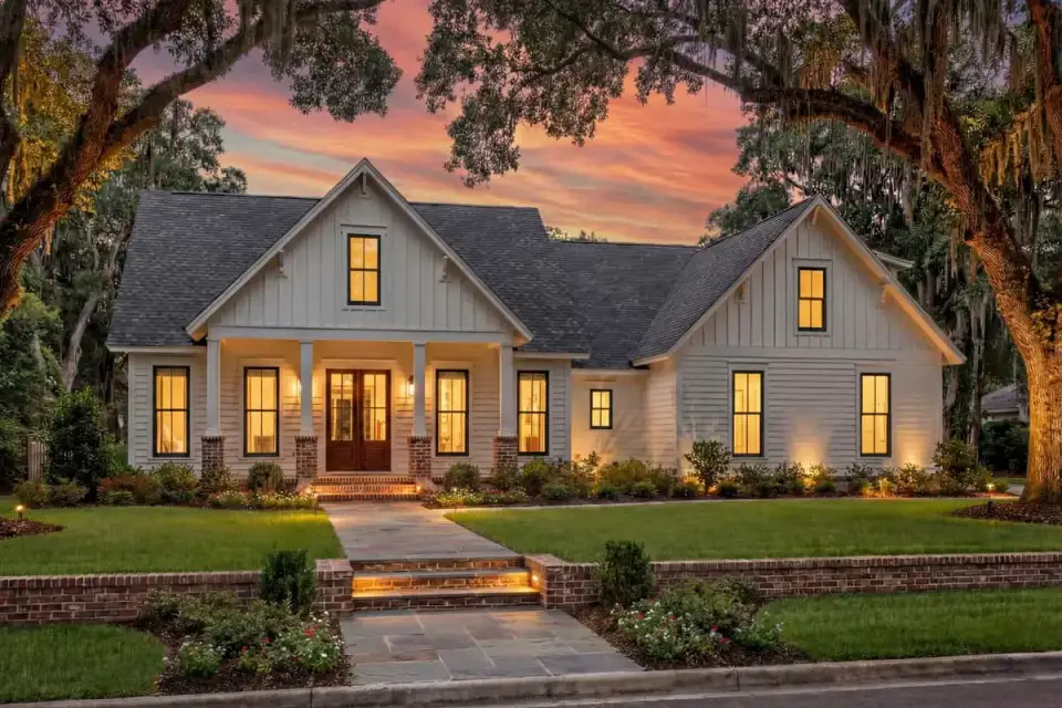 Front elevation of modern farmhouse 51772HZ showing board-and-batten siding, brick column piers, standing-seam metal porch roof, and varied gable rooflines