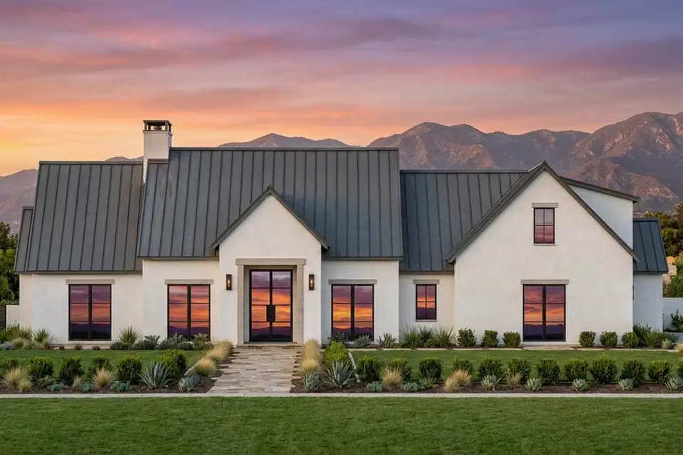 Front rendering of modern transitional house plan 818204JSS with white stucco, steep gables, dark standing-seam metal roof and black-framed windows at sunset