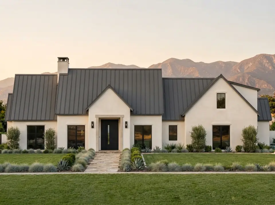 Warm white stucco facade of plan 818204JSS with graphite standing-seam roof, black windows, black front door and silver grasses along a flagstone walk